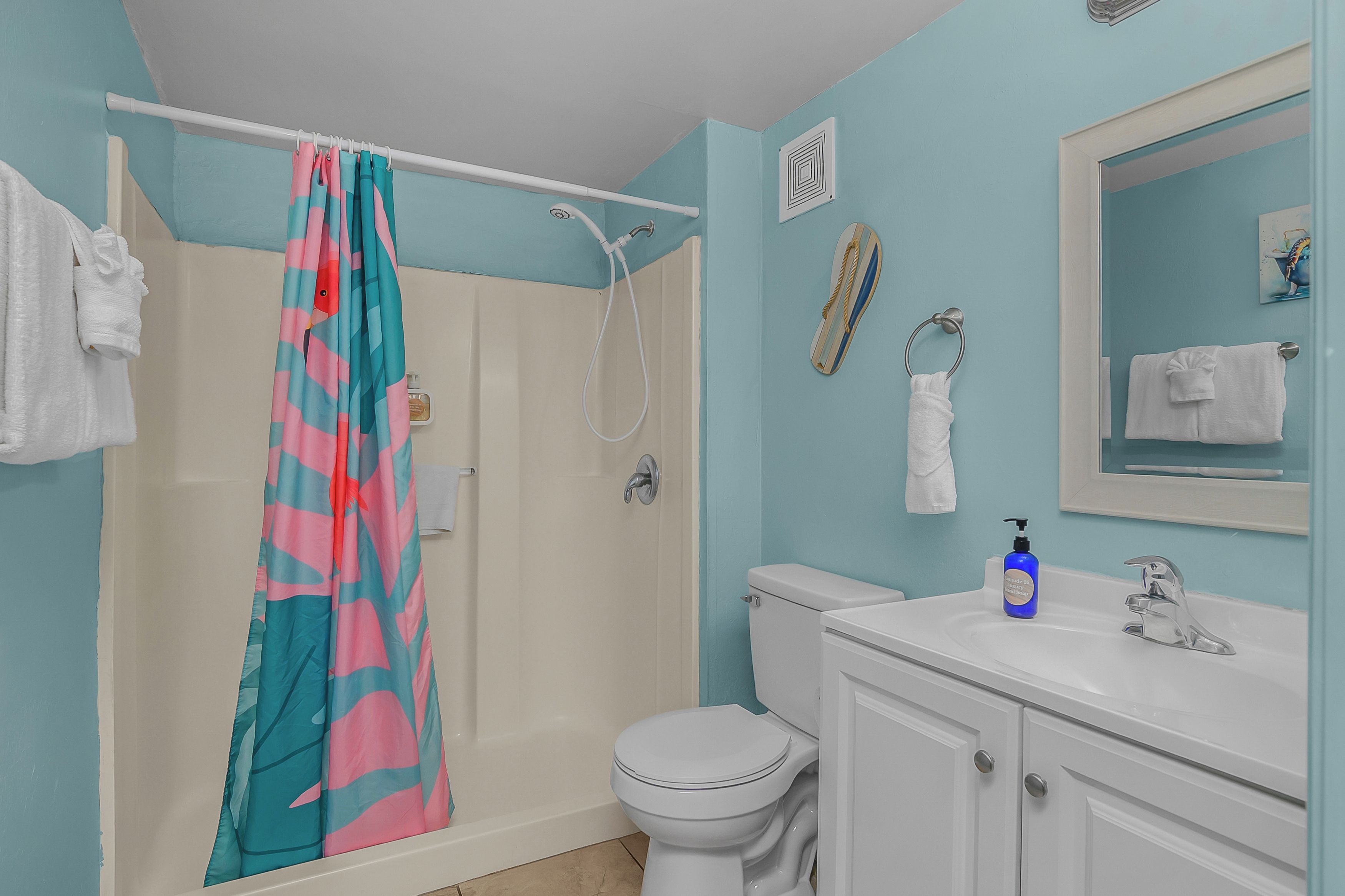 Une salle de bain avec un rideau de douche, des toilettes, un lavabo avec un distributeur de savon et un miroir.