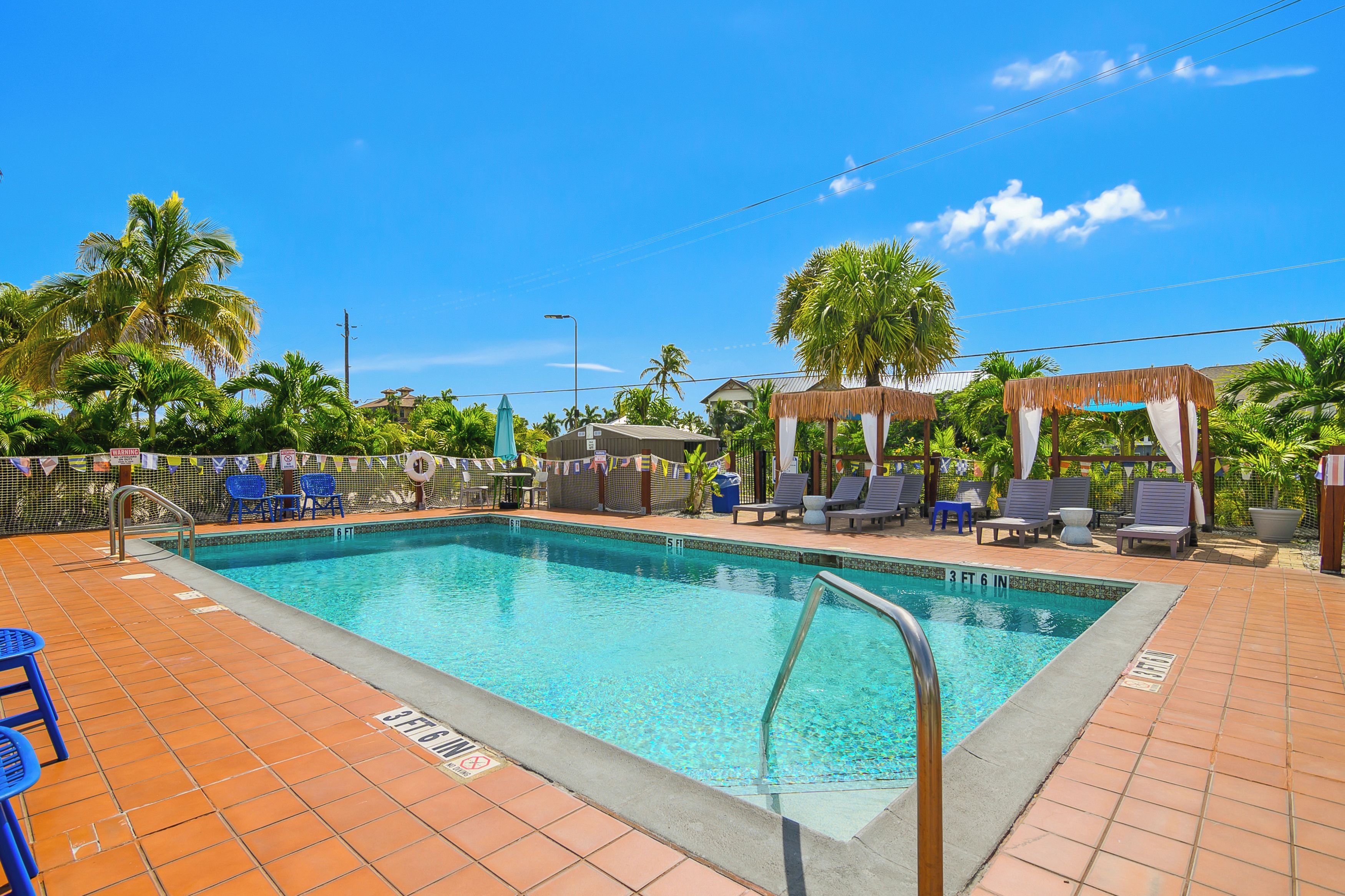 Une piscine avec une terrasse carrelée, des chaises longues et des palmiers.