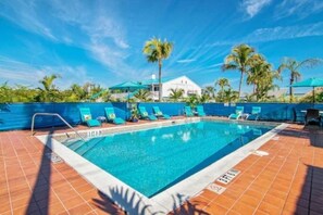 A rectangular swimming pool with a tiled deck, surrounded by palm trees and a white building with a blue roof. - Tropical Two Queen Bed Room at Fort Myers Beach (Fort Myers Beach)