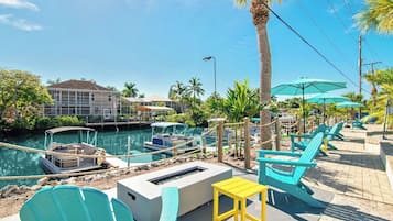 A waterfront area with boats docked, outdoor seating, and a building in the background.