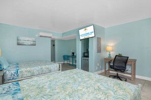A hotel room with two beds, a desk, a chair, a TV, and a sign indicating it's a Latitude 26 Waterfront Resorts location. - Tropical Two Queen Bed Room at Fort Myers Beach (Fort Myers Beach)