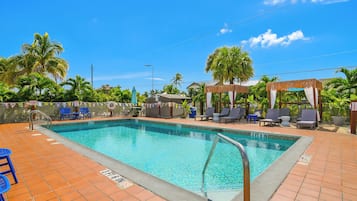 A swimming pool with a tiled deck, lounge chairs, and palm trees.