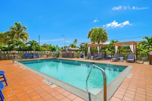 A swimming pool with a tiled deck, lounge chairs, and palm trees. - Tropical King Studio in Fort Myers Beach (Fort Myers Beach)