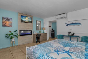 A hotel room with a bed, desk, chair, potted plant, and a wall-mounted TV. - Tropical King Studio in Fort Myers Beach (Fort Myers Beach)