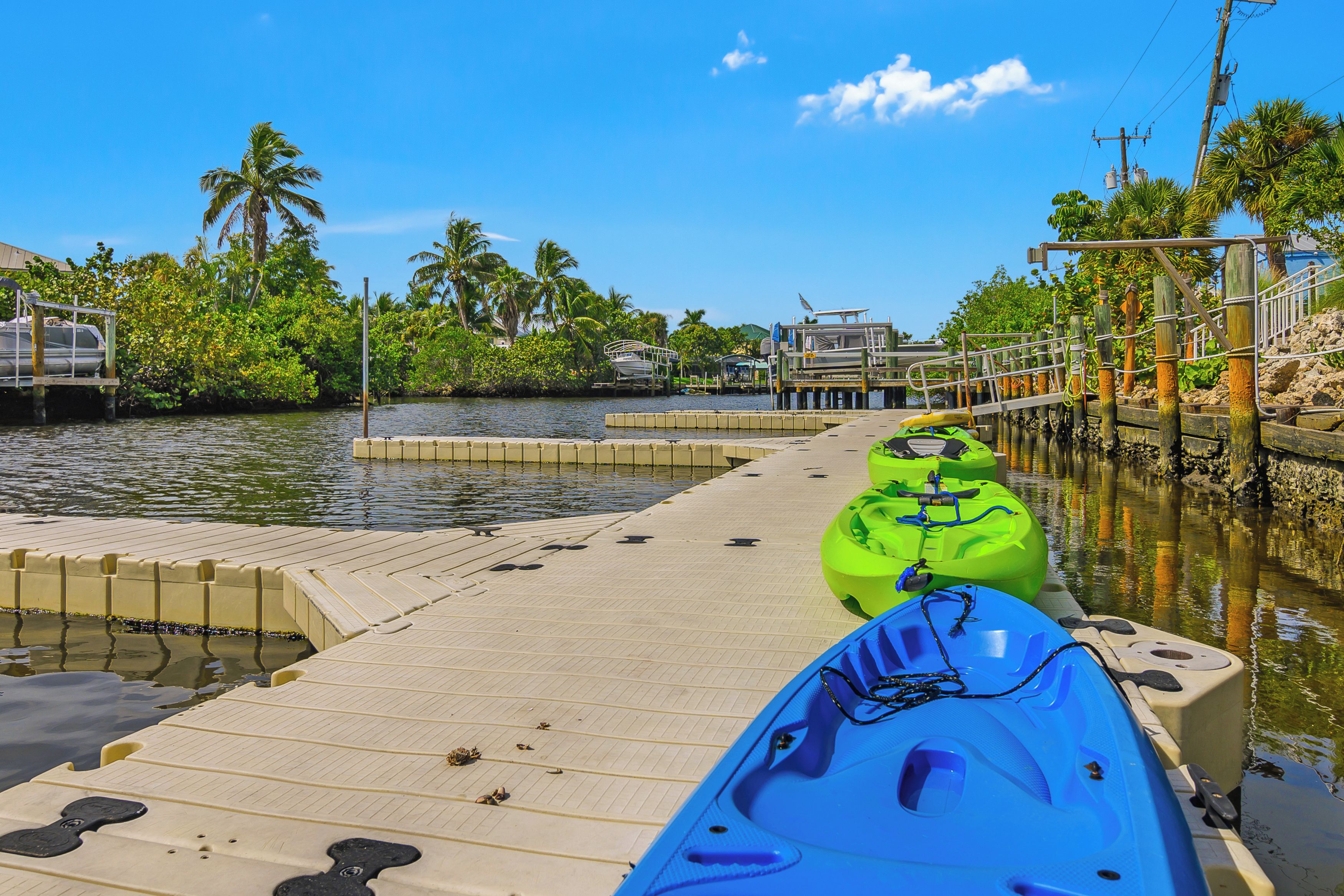 A dock with kayaks and a calm water body, surrounded by greenery and a clear sky.