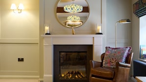 A living room with a fireplace, a brown leather armchair, a round mirror, and a floor lamp. - The Dovecote (Matlock)