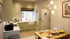 A kitchen with a dining area, a microwave, a sink, and a clock on the wall. - The Dovecote (Matlock)