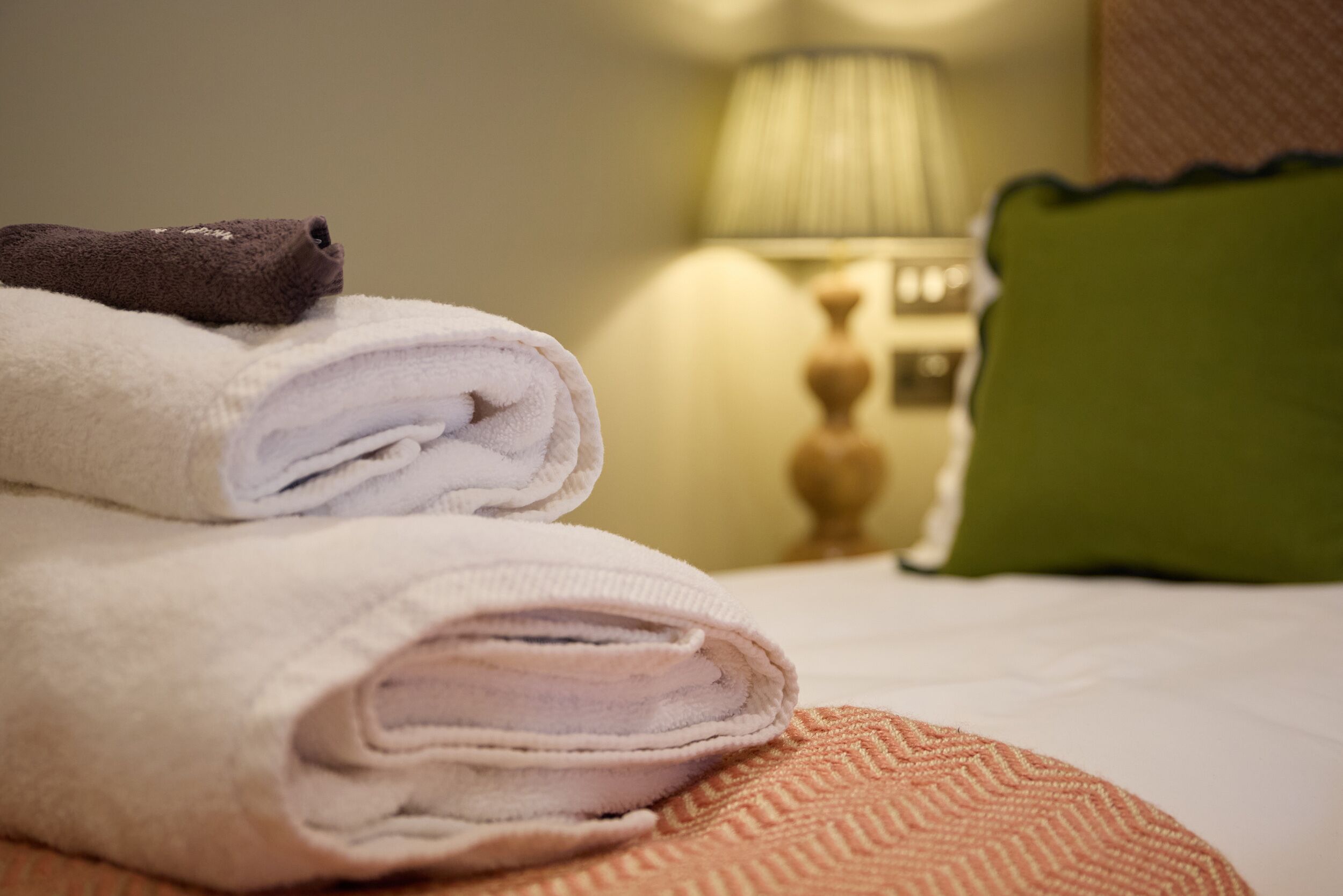 A neatly made bed with folded towels and a green pillow.