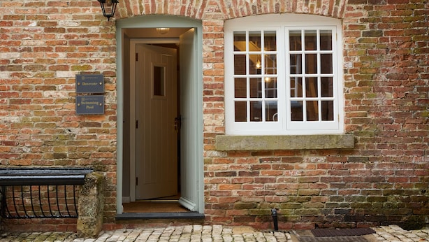 A brick building with a white-framed window and a door leading to an interior. There is a sign on the wall indicating a swimming pool. - The Dovecote (Matlock)