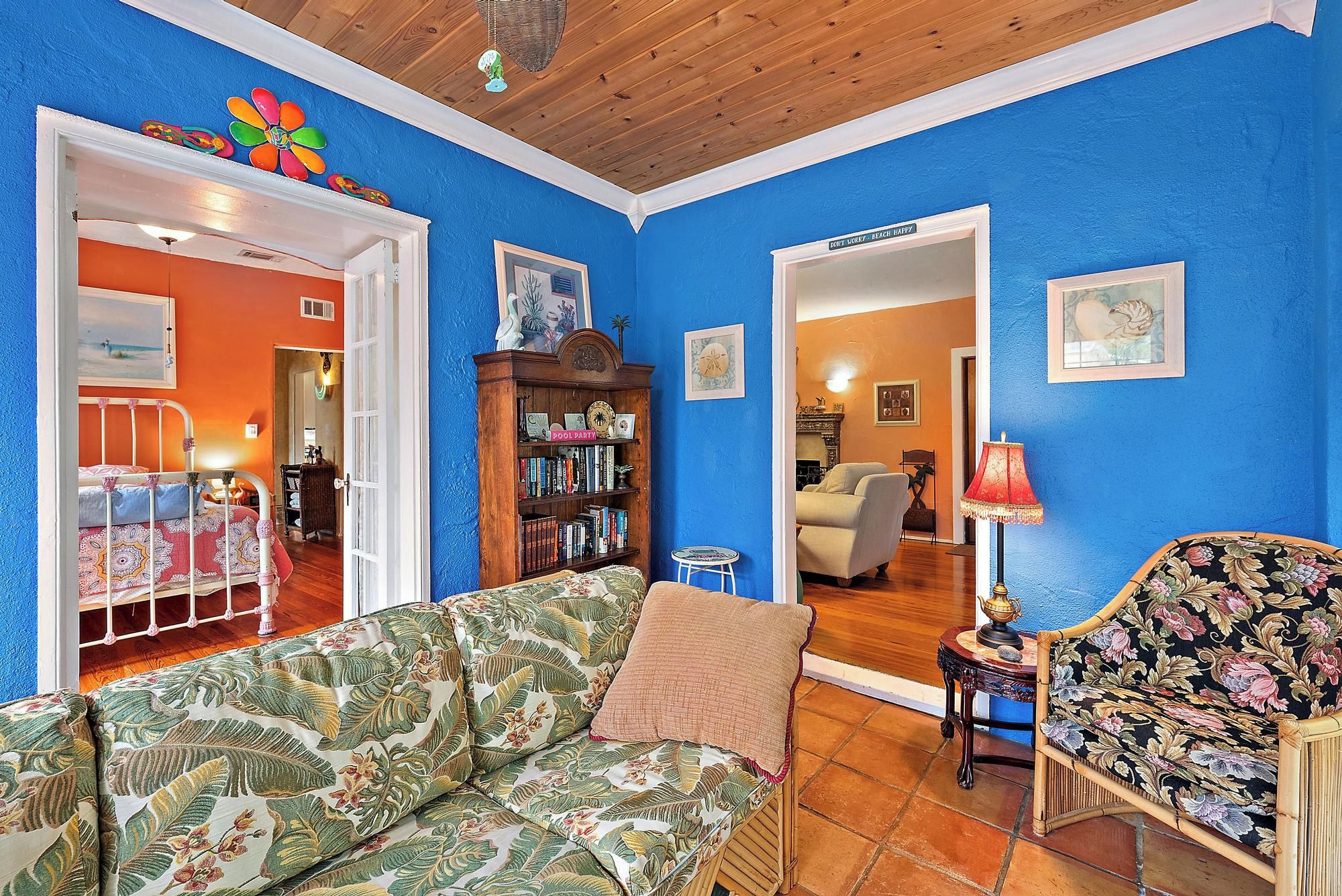 Ein Wohnzimmer mit blauer Wand, Holzboden, einem Blumensofa, einem Bücherregal aus Holz und einem Stuhl mit floralem Muster.