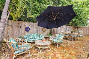 Une terrasse extérieure avec des meubles en osier, une table ronde et un grand parasol.