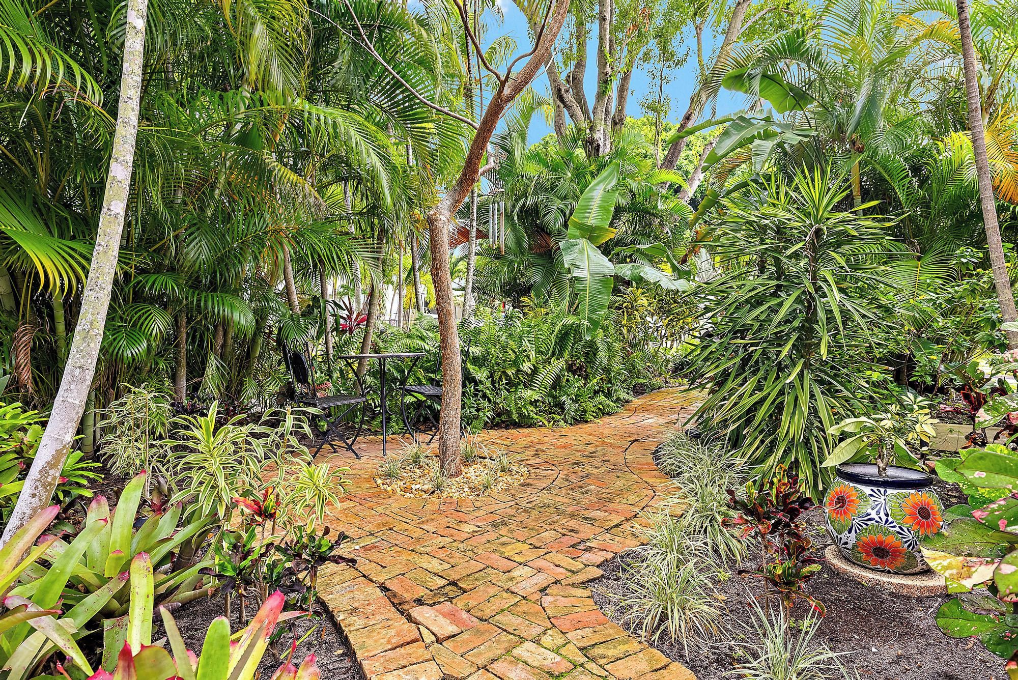 Un jardin avec un chemin en briques, différentes plantes et un pot de fleurs décoratif.