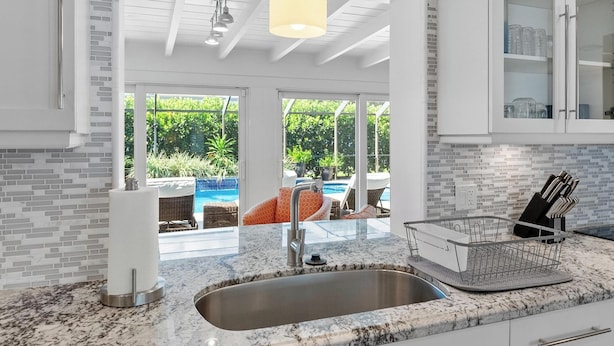 A modern kitchen with a large window, a sink, and a hanging light fixture. - Bimini Breeze - Updated Island Retreat with Pool & Beach Access (West Palm Beach)