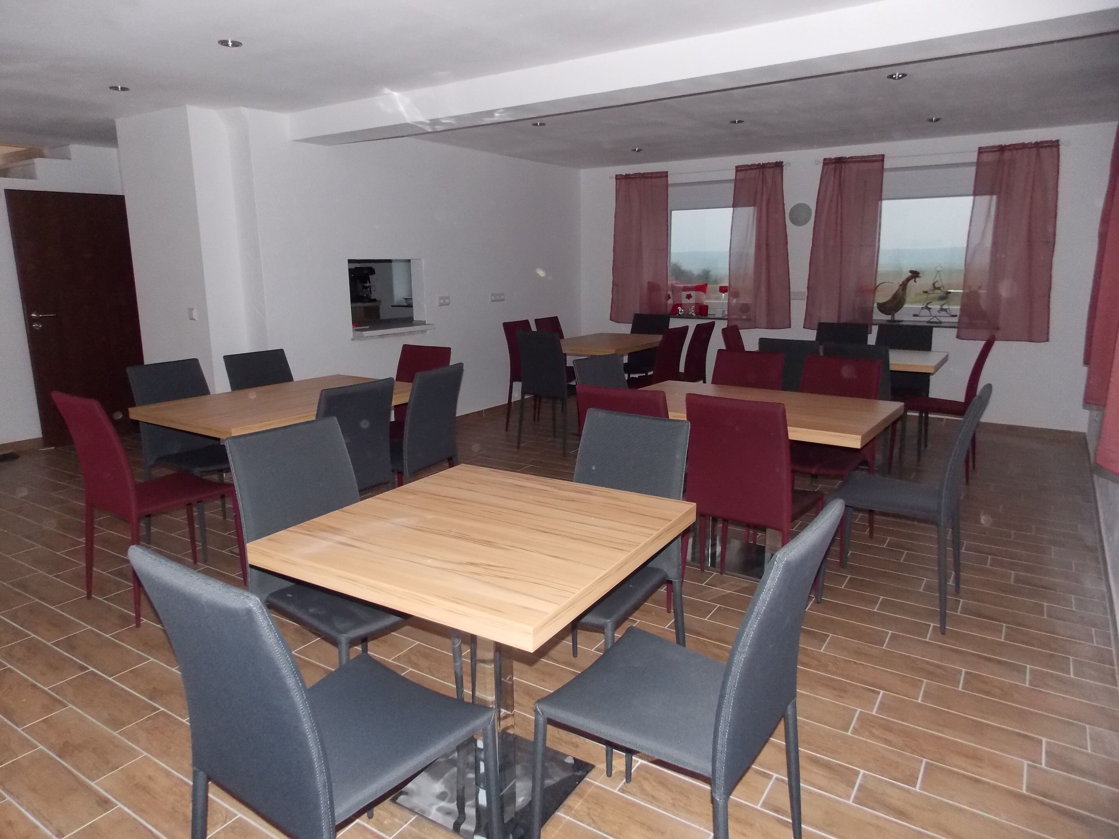 Un espace repas comprenant plusieurs tables et chaises, un téléviseur et une fenêtre avec des rideaux.