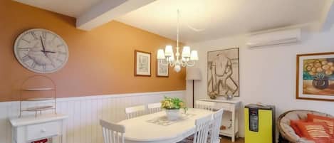 A dining area with a white table, chairs, a clock, and wall art.