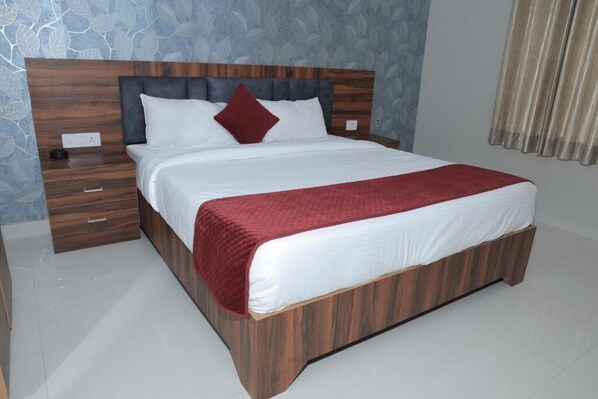 Une chambre d’hôtel avec un lit en bois, du linge de lit blanc, un plaid rouge et une table de chevet avec une lampe.