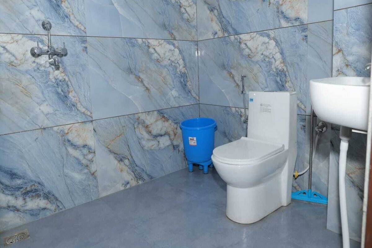 Une salle de bain avec un mur en marbre, des toilettes, un lavabo et une poubelle bleue.