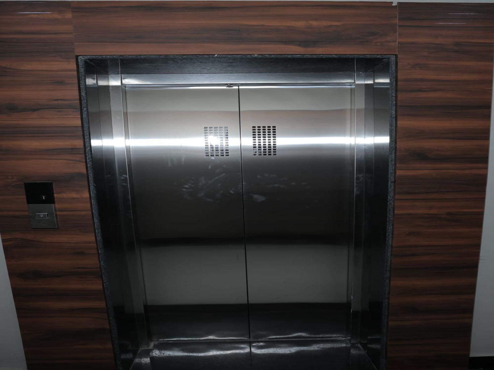 En moderne elevator med metalfinish og et kontrolpanel på venstre side.