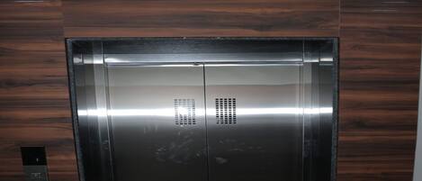 En moderne elevator med metalfinish og et kontrolpanel på venstre side.