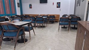 A restaurant with marble flooring, wooden tables and chairs, and a wooden bench area. - Hotel Om Palace (Jaipur)