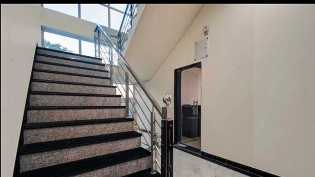 A staircase with black steps and a metal railing, leading to a room with a white wall and a door. - Hotel Om Palace (Jaipur)
