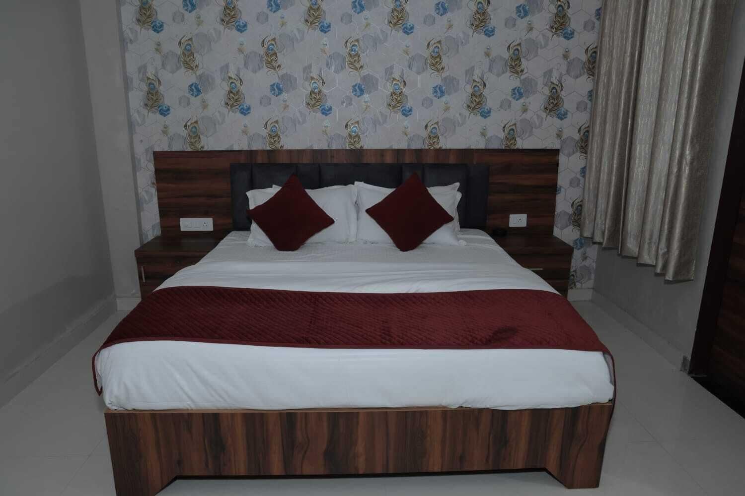 A neatly made bed with a wooden headboard, white bedding, and two red pillows.