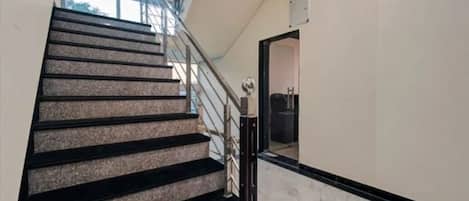 A staircase with black steps and a metal railing, leading to a room with a white wall and a door.