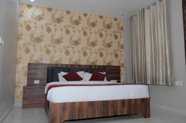 Un dormitorio con cabecera de madera, una cama con ropa de cama blanca y almohadas rojas, una mesita de noche y un papel tapiz estampado.