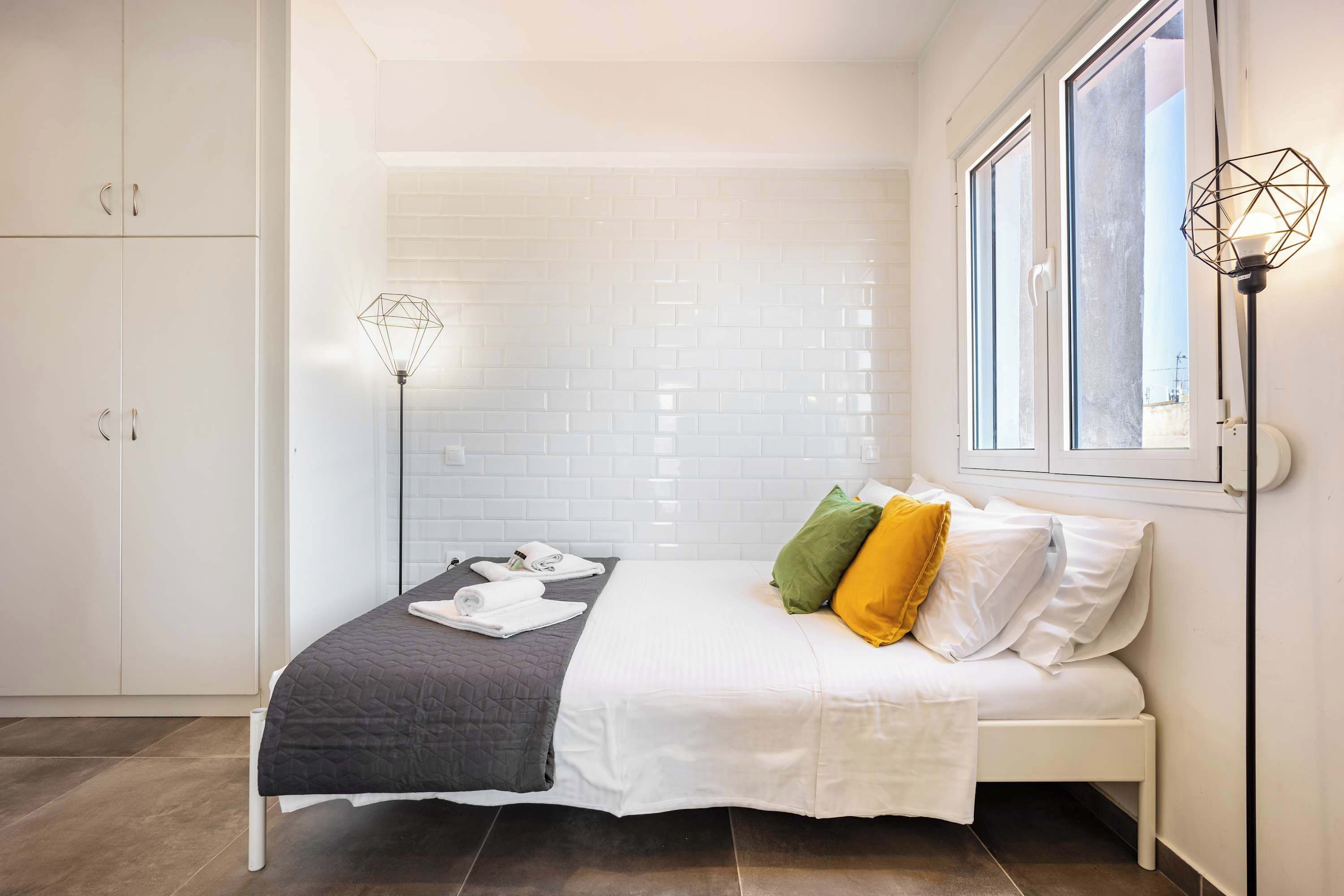 A neatly arranged bedroom with a bed, pillows, a bedside lamp, and a window with a view.