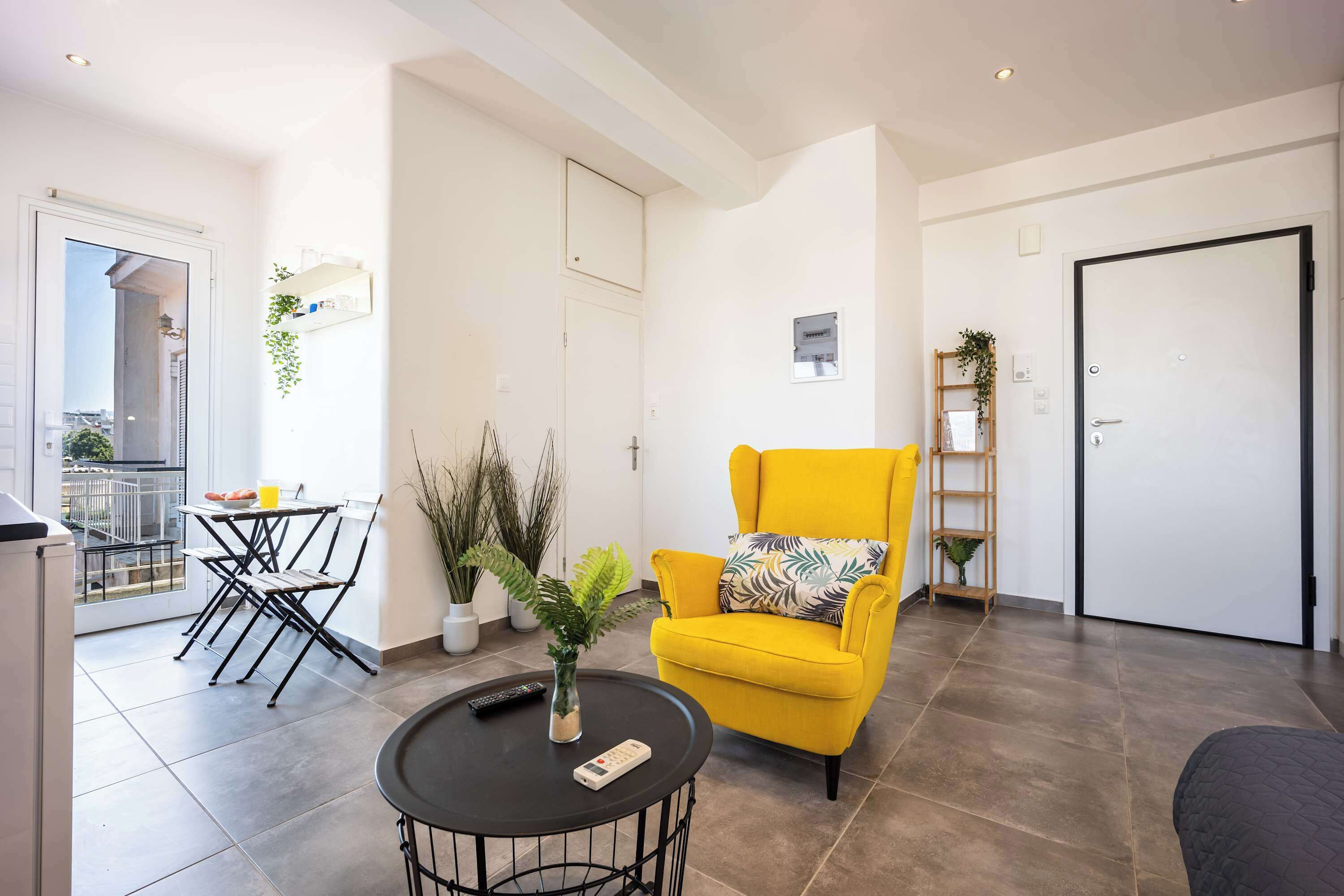 A modern living room with a yellow armchair, a round coffee table, and a dining area with a small table and chairs.