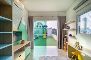 Une salle de jeux moderne pour enfants, équipée d’un téléviseur, d’étagères et offrant une vue sur un espace de jeux extérieur.