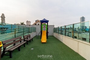 Une aire de jeux sur le toit, avec un toboggan, des bancs et une rambarde en verre.