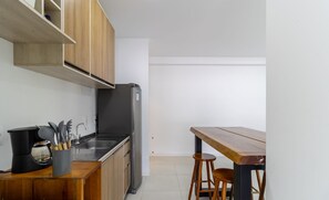 A compact kitchen with a refrigerator, stove, and wooden cabinets. There is a small dining area with a wooden table and two stools. - Apt w/ Swimming Pool Well Located Blumenau Neb0103 (Blumenau)