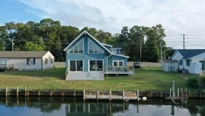 A two-story house with a large front porch and a dock extending into a body of water.