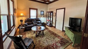 A living room with a leather sofa, a coffee table, a TV, and a bookshelf. - Glenrock Cottage -  charming 4-bedroom house in Glenrock WY (Glenrock)