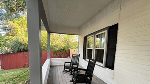 A covered porch with a wooden floor, a red fence, and a view of trees and a wooden deck in the background. - Glenrock Cottage -  charming 4-bedroom house in Glenrock WY (Glenrock)