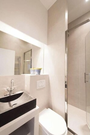 A modern bathroom with a black sink, a white toilet, and a glass shower enclosure. - STEP INTO TIMELESS PARISIAN CHARM IN THE VIBRANT HISTORIC LE MARAIS -RUE CHARLOT (Paris)