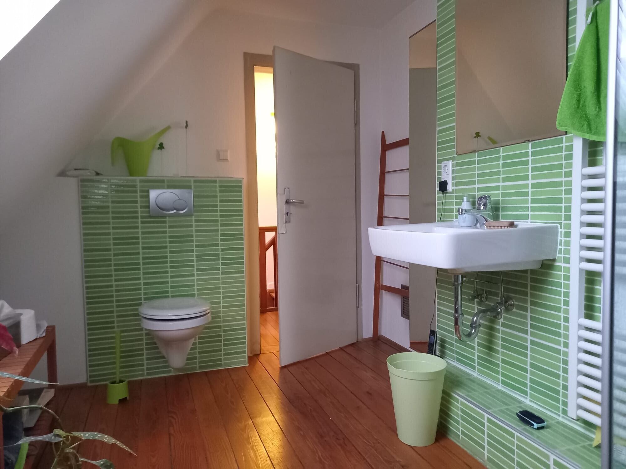 A bathroom with a toilet, sink, and green tiled walls.