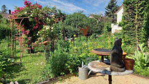A garden with a metal sculpture, a metal watering can, and a variety of plants.
