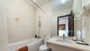 Une salle de bain équipée d’une baignoire, de toilettes, d’un lavabo et d’un sèche-cheveux fixé au mur.