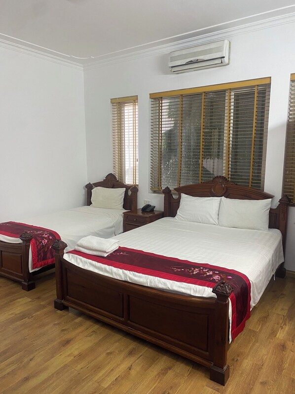 A double bed with a wooden frame and a red and white bedspread, two bedside tables, and an air conditioning unit above the windows.