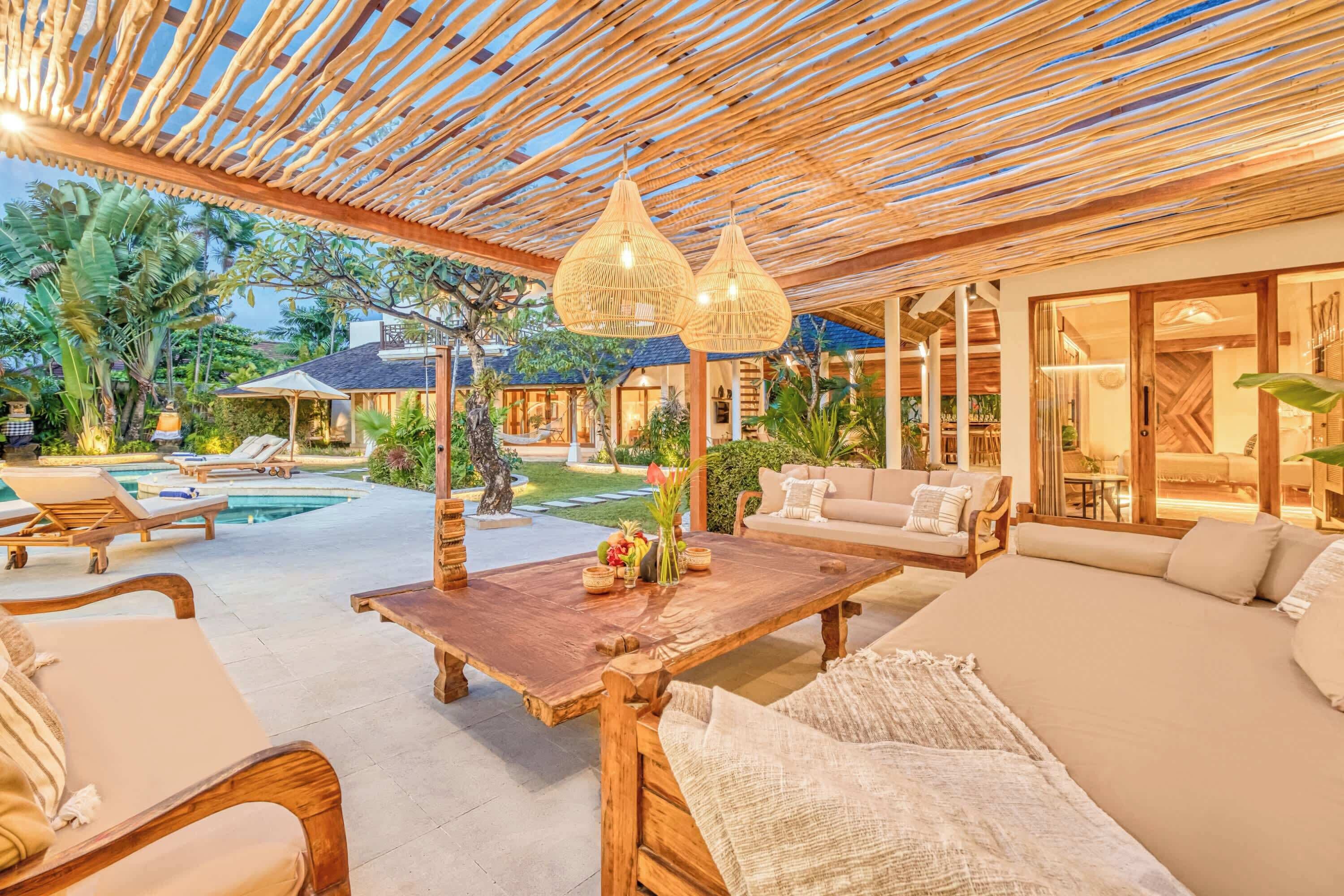 Uma área externa ampla com pérgola de madeira, cadeiras de descanso, mesa de jantar e piscina.