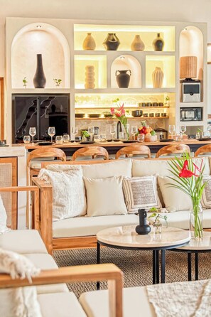 Een moderne woonkamer met een bank, salontafel en een eethoek. Er is een open haard, een televisie en een wand met decoratieve vazen.