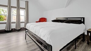Un dormitorio con cama, una silla, una mesita de noche y una ventana con cortinas.
