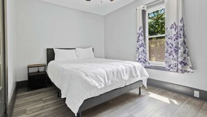 Une chambre à coucher avec un lit, une table de chevet, un ventilateur de plafond et une fenêtre avec des rideaux.