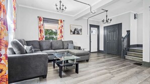 Un salon moderne avec un canapé d’angle gris, une table basse en verre et un lustre.
