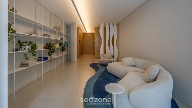 Un interior moderno con un sofá blanco, un tapete azul y estanterías blancas con plantas.