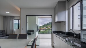 Una cocina moderna con un ventanal grande, un comedor con mesa y sillas, y vista a una ladera verde.