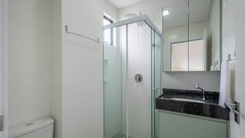 A modern bathroom with a glass-enclosed shower, a toilet, and a sink with a marble countertop.