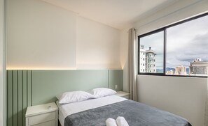 Een hotelkamer met een bed, een nachtkastje, een raam met uitzicht op de stad en een groene wand.
